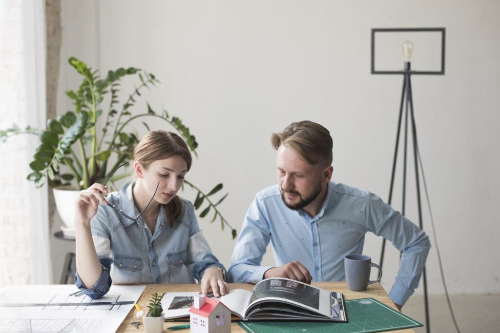 woman-holding-spectacle-looking-interior-catalog-with-her-male-coworker-office