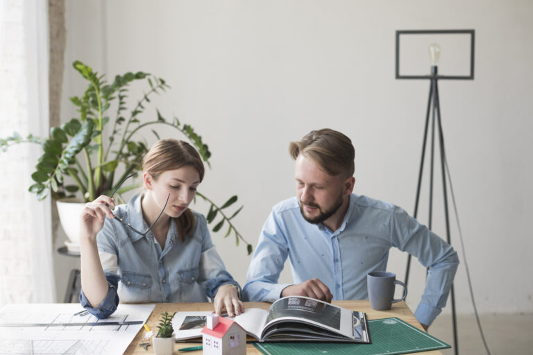 woman-holding-spectacle-looking-interior-catalog-with-her-male-coworker-office